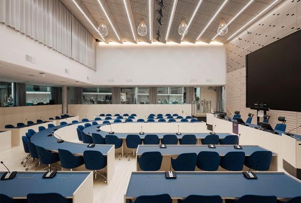 Ein moderner Konferenzraum mit blauen Stühlen und Tischen in einem hellen Gebäude.