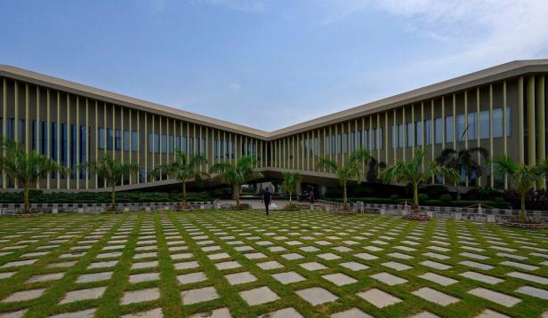 Ein modernes Gebäude mit einem Rasen aus quadratischen Steinplatten und Palmen im Vordergrund.