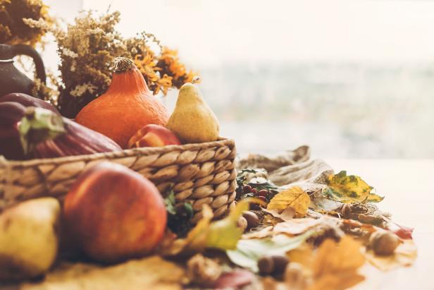 Ein Korb mit Herbstfrüchten und Gemüse, umgeben von bunten Blättern.