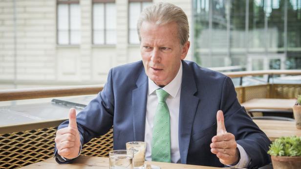 Ein Mann im Anzug sitzt an einem Tisch und gestikuliert.