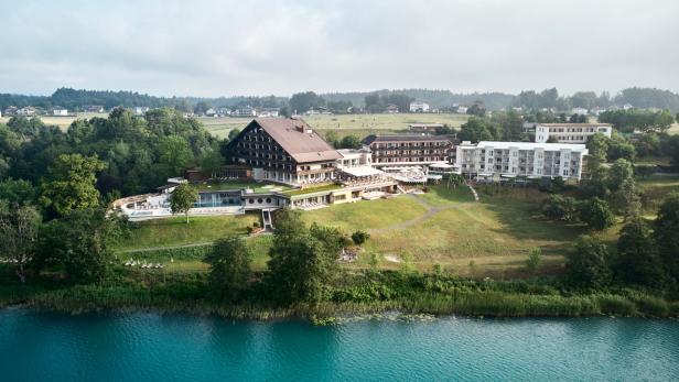 Ein Hotelresort liegt an einem Seeufer mit türkisfarbenem Wasser.