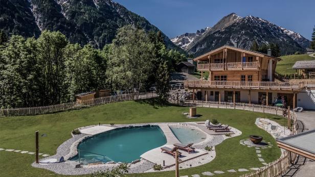 Ein Holzhaus mit Pool und Liegestühlen vor einer Bergkulisse.
