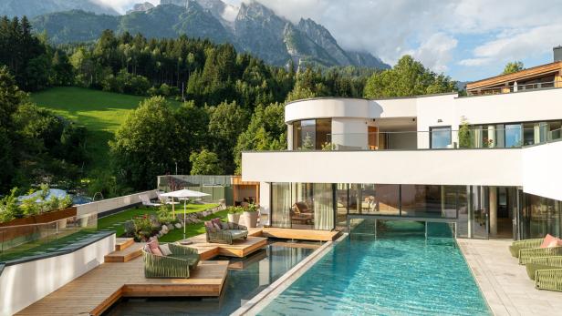 Ein modernes Haus mit Pool vor einer Bergkulisse.