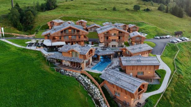 Luftaufnahme eines luxuriösen Resorts mit Holzhäusern und einem Pool in einer grünen Hügellandschaft.