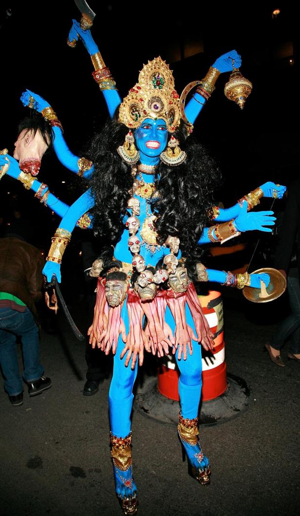 Eine Person in einem aufwendigen, blau gefärbten Kali-Kostüm mit mehreren Armen und goldenem Schmuck.