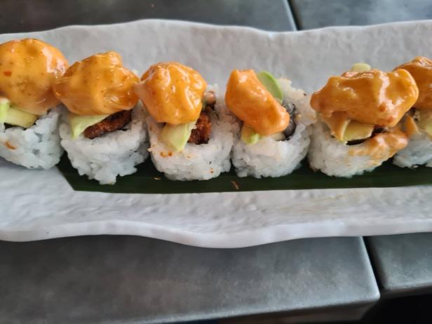 Eine Reihe von Sushi-Rollen mit Avocado und einer cremigen, orangefarbenen Sauce auf einem Teller.