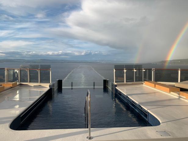Ein Regenbogen erstreckt sich über das Meer, gesehen von einem Pooldeck aus.