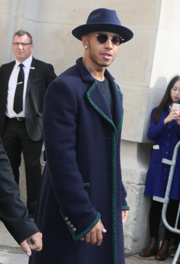Lewis Hamilton trägt einen blauen Hut und einen passenden Mantel mit grünen Akzenten.