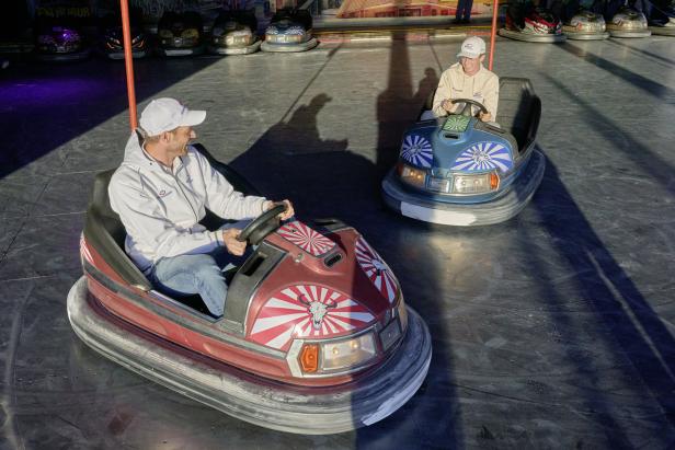 Zwei Personen fahren in bunten Autoscootern auf einem Jahrmarkt.