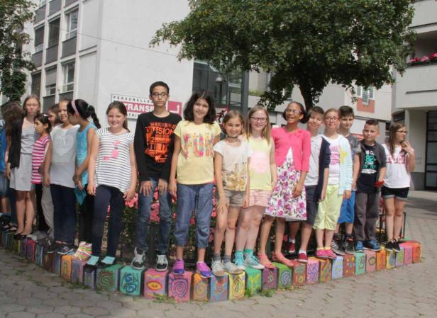 Eine Gruppe von Schulkindern steht auf einer bunten Mauer vor einem Gebäude.