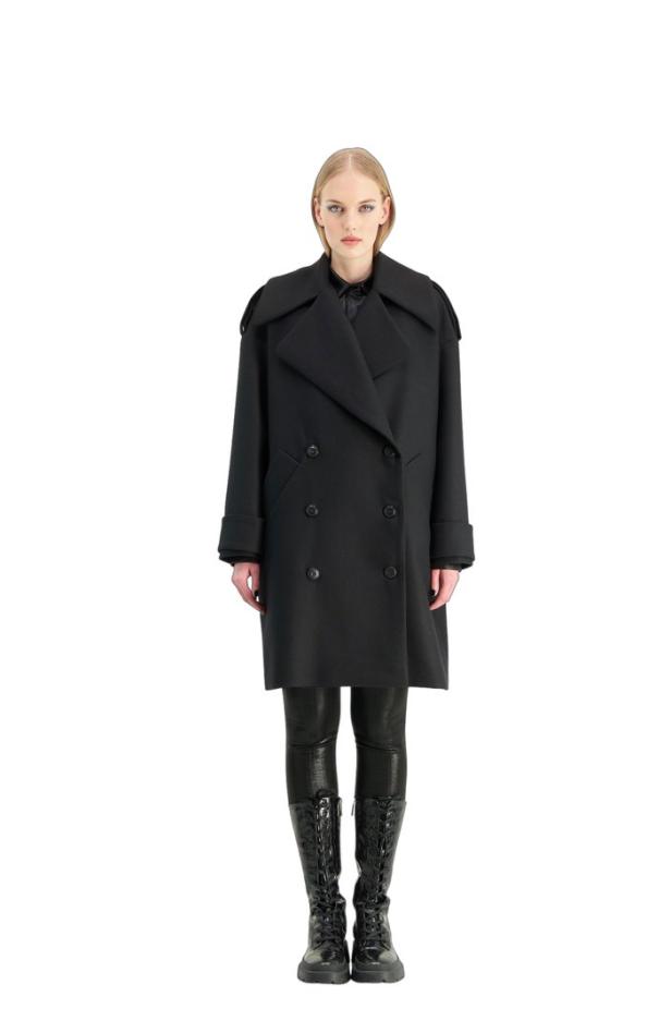 Eine Frau trägt einen schwarzen zweireihigen Mantel und glänzende Stiefel.