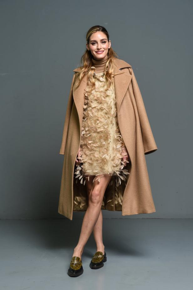Olivia Palermo trägt einen beigen Mantel und ein Federkleid.
