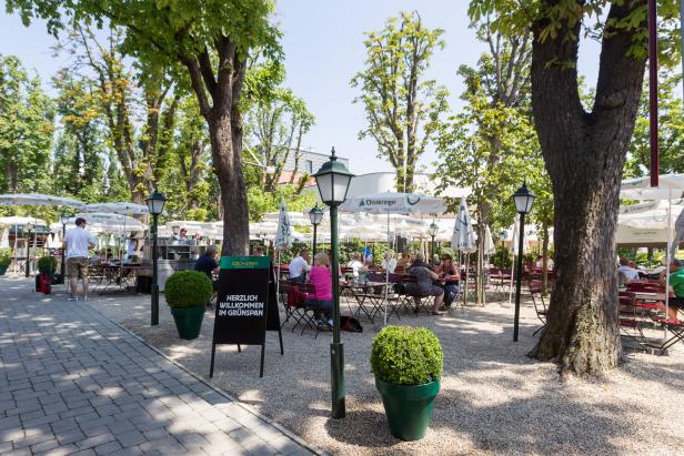 Einladender Biergarten im Grünen mit Gästen unter Sonnenschirmen.