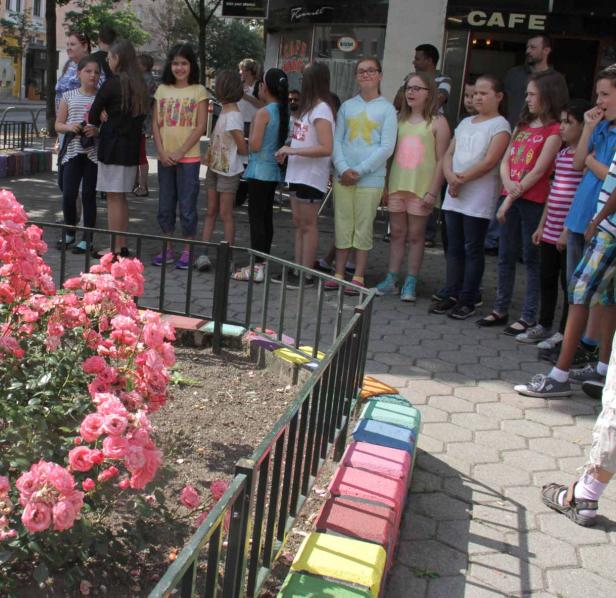 Eine Gruppe Kinder steht vor einem Café, hinter einem kleinen Beet mit Rosen.