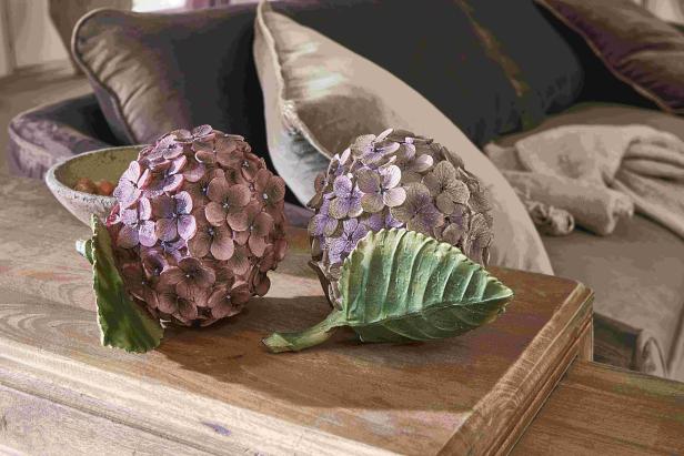 Zwei künstliche Hortensienblüten liegen auf einem Holztisch.