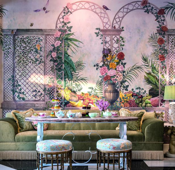 Ein gedeckter Tisch mit Teegeschirr und Gebäck vor einer Wandmalerei mit Blumen und Früchten.
