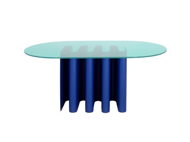Ein ovaler Tisch mit einer türkisfarbenen Glasplatte und einem blauen, geriffelten Säulenfuß.