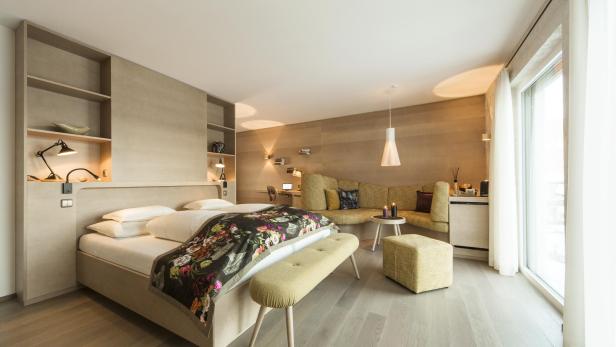Ein helles Hotelzimmer mit Bett, Sofa und Schreibtisch.