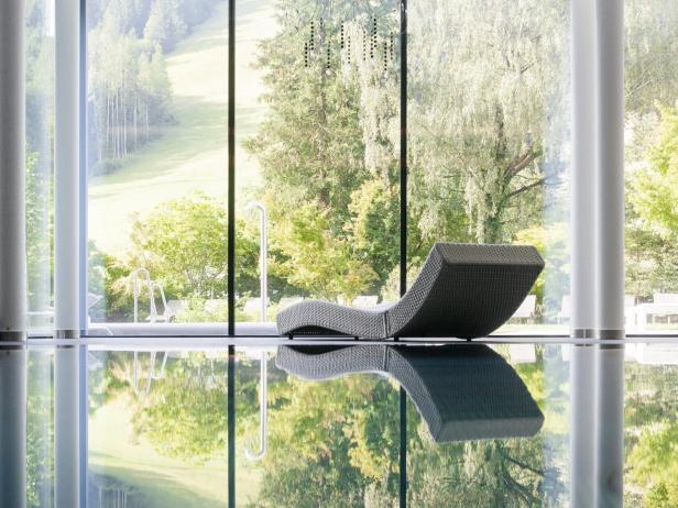 Ein grauer Liegestuhl steht am Rande eines Pools mit Blick auf eine grüne Landschaft.