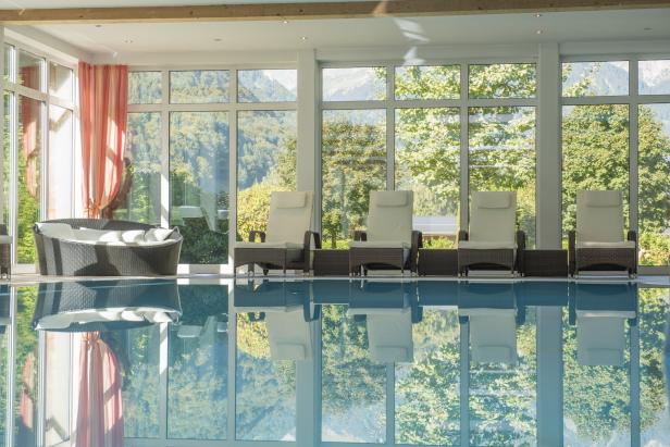 Ein Innenpoolbereich mit Liegestühlen und Blick auf eine bewaldete Berglandschaft.