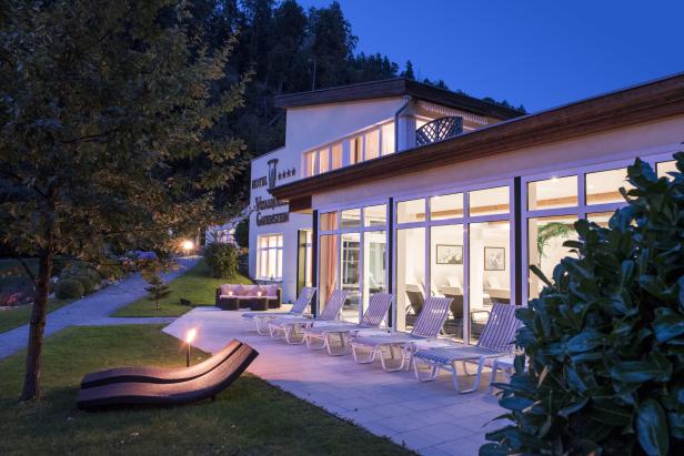 Das Hotel Vitalquelle Gaderstein mit Liegestühlen im Außenbereich bei Dämmerung.