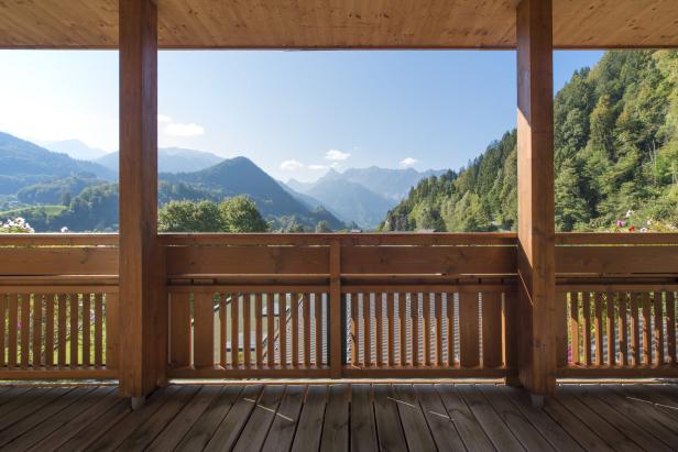 Blick von einem Holzbalkon auf eine grüne Berglandschaft.