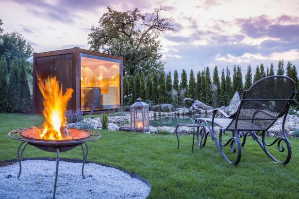 Ein Garten mit Sauna, Feuerstelle und Teich bei Dämmerung.