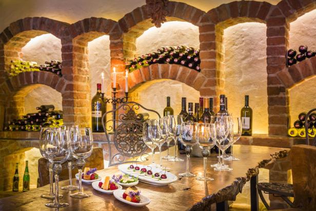 Ein gedeckter Tisch mit Wein, Gläsern und kleinen Speisen in einem Weinkeller.