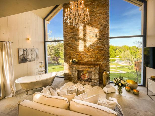 Ein luxuriöses Wohnzimmer mit Kamin, Badewanne und Blick auf einen Garten.