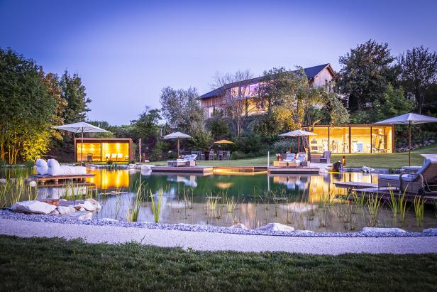 Ein luxuriöses Resort mit einem See, kleinen Häusern und Liegeflächen im Freien bei Dämmerung.