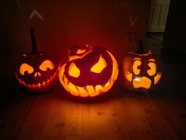 Drei geschnitzte Halloween-Kürbisse stehen auf einem Holzboden und leuchten.