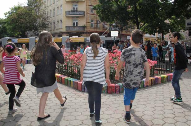 Eine Gruppe Kinder tanzt auf einem Platz in der Stadt.