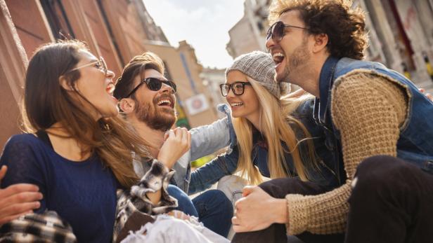 Eine Gruppe junger Leute sitzt im Freien und lacht.