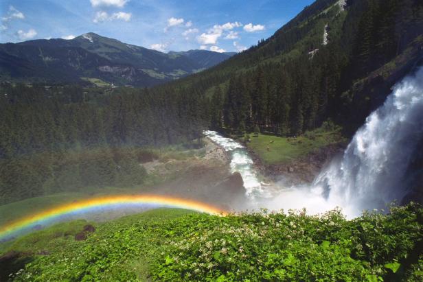 Ein Regenbogen spannt sich vor einem Wasserfall in einer grünen Landschaft.