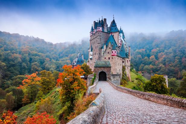 Die Burg Eltz thront auf einem Hügel, umgeben von herbstlichen Wäldern.