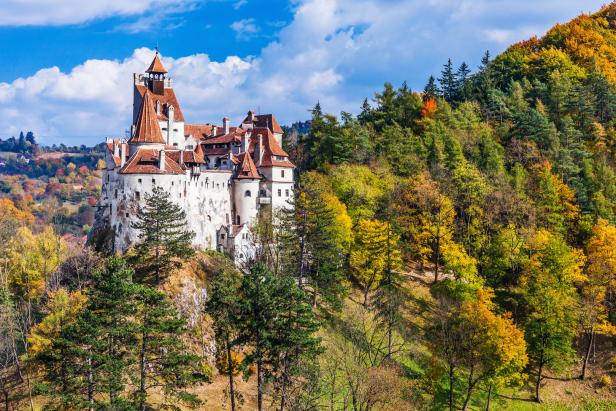 Schloss Bran thront auf einem Hügel inmitten einer herbstlichen Waldlandschaft.