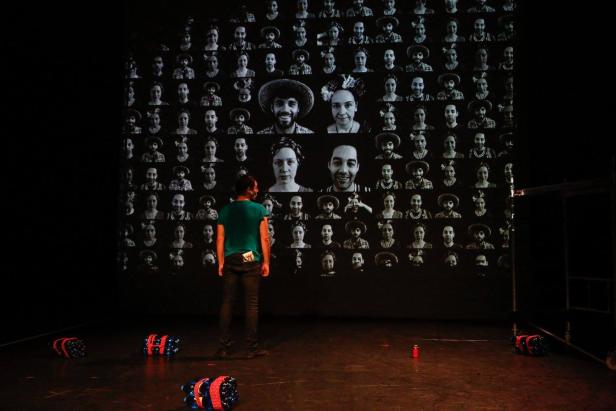 Ein Mann steht vor einer Leinwand mit vielen schwarz-weißen Porträts von Menschen.