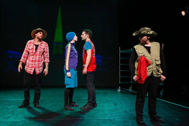 Vier Schauspieler stehen auf einer Bühne vor einem dunklen Hintergrund.