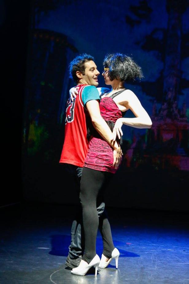 Ein Mann im Basketballtrikot umarmt eine Frau mit schwarzer Perücke auf einer Bühne.