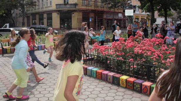 Eine Gruppe Mädchen spielt auf einem Platz mit einem Rosenbeet und bunten Betonblöcken.
