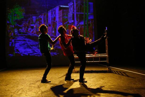 Drei Darsteller in farbenfroher Beleuchtung auf einer Bühne.