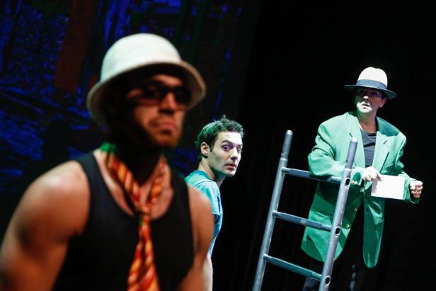 Drei Schauspieler stehen auf einer Bühne vor einer Leiter.
