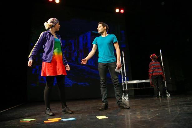 Zwei Schauspieler stehen auf einer Bühne vor einem Bühnenbild.