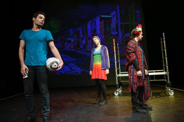 Drei Schauspieler stehen auf einer Bühne vor einer Projektion mit einem Fußball und Leitern.