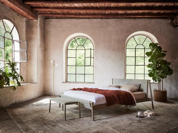 Ein Schlafzimmer mit einem Bett, zwei großen Fenstern und Zimmerpflanzen.