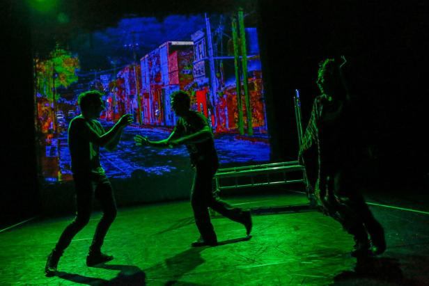 Drei Personen stehen auf einer Bühne vor einer farbenfrohen Projektion einer Stadtansicht.