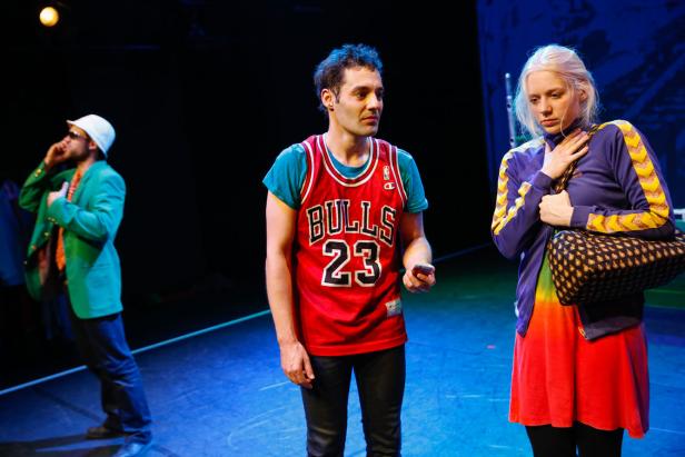 Drei Schauspieler stehen auf einer Bühne, der mittlere trägt ein Bulls-Trikot.