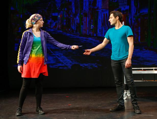 Auf einer Bühne überreicht eine Frau einem Mann einen Gegenstand.