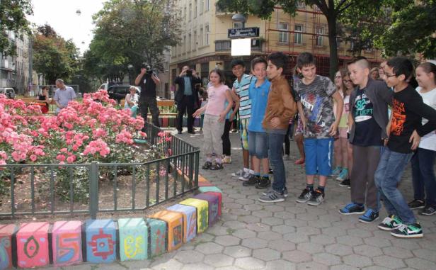 Eine Gruppe von Kindern steht vor einem Rosenbeet in der Nähe des B. Friedensreich Hundertwasser Platzes.