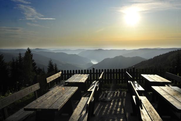Ein Panoramablick von einer hölzernen Picknickbank auf eine Hügellandschaft im Abendlicht.